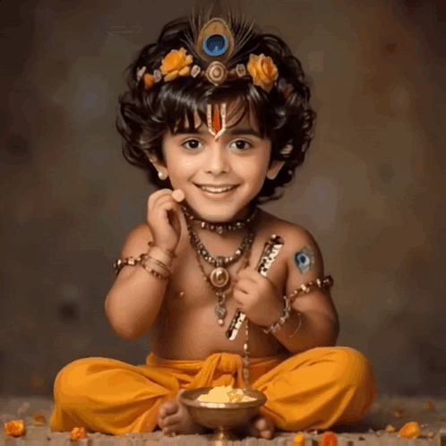 A Little Boy Dressed As Krishna Is Sitting On The Ground With A Bowl Of Food GIF