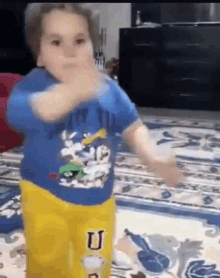 A Little Boy In A Blue Shirt And Yellow Pants Is Dancing On A Rug . GIF