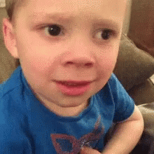 A Little Boy In A Blue Shirt Is Sitting On A Couch . GIF