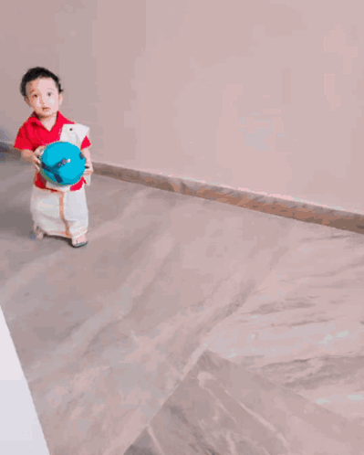 A Little Boy In A Red Shirt And White Pants Holds A Blue Ball GIF