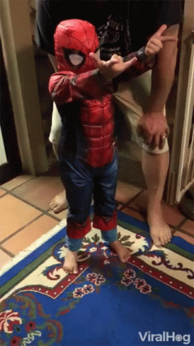 A Little Boy In A Spiderman Costume Is Standing On A Blue Rug GIF