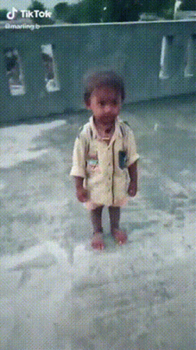 A Little Boy In A Yellow Shirt Is Standing In A Puddle Of Water GIF