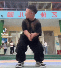 A Little Boy Is Dancing In Front Of A Building That Says Tiktok GIF