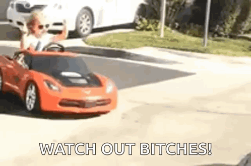 A Little Boy Is Driving A Toy Car Down The Street . GIF