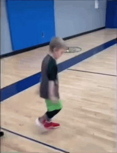A Little Boy Is Jumping On A Wooden Basketball Court . GIF