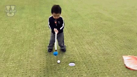 A Little Boy Is Laying On The Ground On A Golf Course Next To A Flag And A Golf Club . GIF