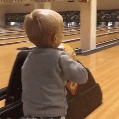 A Little Boy Is Playing In A Bowling Alley With A Bowling Ball . GIF