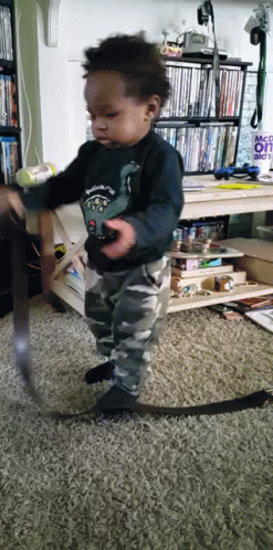 A Little Boy Is Playing With A Remote Control In Front Of A Sign That Says " Make It " GIF
