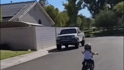 A Little Boy Is Riding A Motorcycle Down A Street GIF