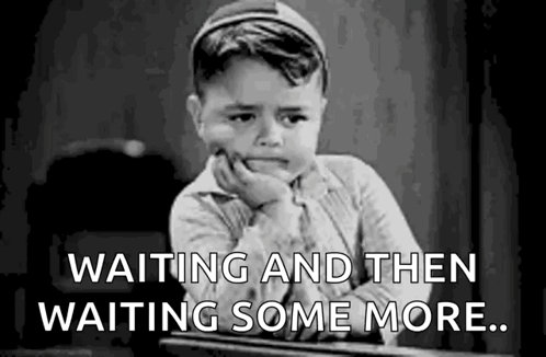 A Little Boy Is Sitting At A Desk With His Hand On His Chin And The Words `` Waiting And Then Waiting Some More '' . GIF