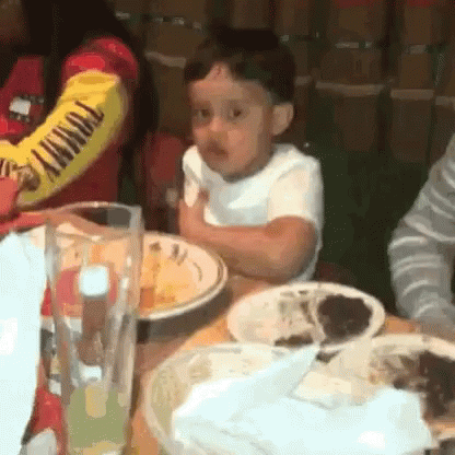 A Little Boy Is Sitting At A Table With Plates Of Food And A Glass Of Beer . GIF