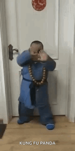 a little boy is standing in front of a door wearing a blue robe and a necklace of beads .
