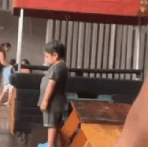 A Little Boy Is Standing In Front Of A Red Canopy . GIF