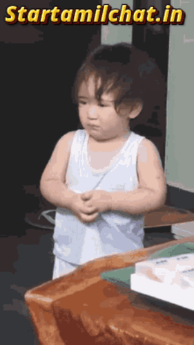 a little boy is standing in front of a wooden table with the words starttamilchat.in written above him