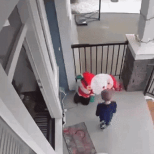 A Little Boy Is Standing Next To A Stuffed Santa Claus In A House . GIF
