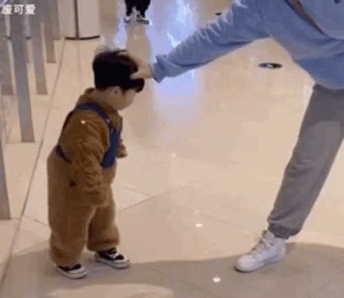 A Little Boy Is Standing Next To A Woman And Touching Her Head . GIF
