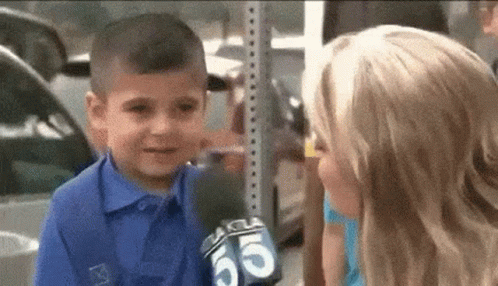 A Little Boy Is Talking To A Girl With A Microphone In His Hand . GIF