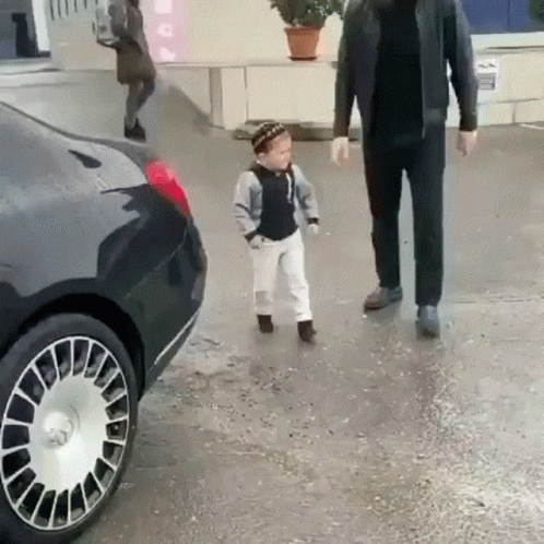 A Little Boy Is Walking Next To A Man In A Black Jacket . GIF