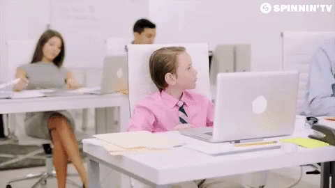 A Little Boy Sitting At A Desk With An Apple Laptop On It GIF