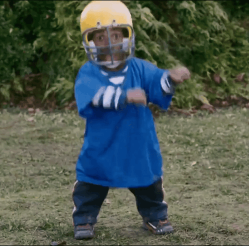 A Little Boy Wearing A Blue Shirt And A Yellow Helmet Is Dancing GIF