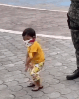 A Little Boy Wearing A Face Mask Is Standing On A Brick Sidewalk . GIF