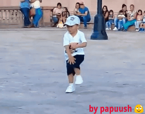 A Little Boy Wearing A Hat And A White Shirt Is Running On The Street GIF