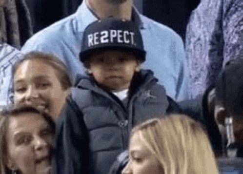 A Little Boy Wearing A Hat That Says Respect Is Sitting In The Stands . GIF