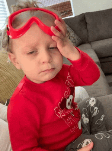 A Little Boy Wearing A Red Shirt With Mickey Mouse On It Is Rubbing His Forehead GIF
