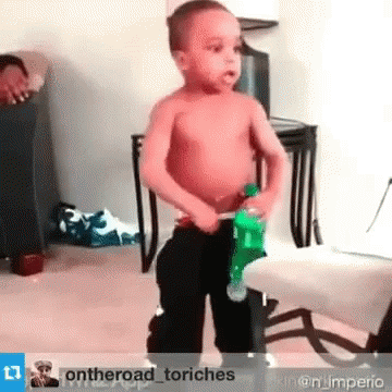 A Little Boy Without A Shirt Is Holding A Green Bottle Of Soda . GIF