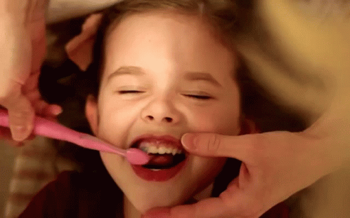 A Little Girl Brushing Her Teeth With A Pink Brush GIF