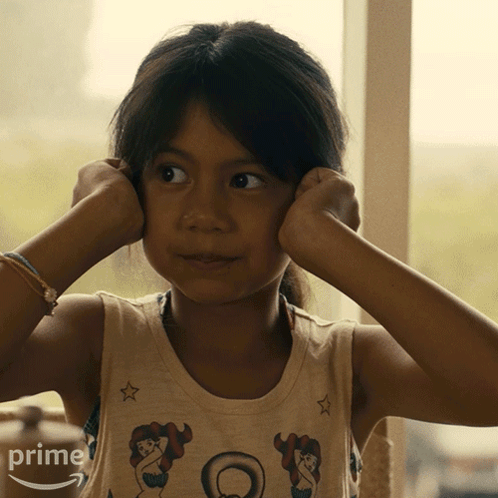 A Little Girl Covering Her Ears With Her Hands And A Shirt That Says Prime On It GIF
