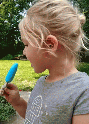 A Little Girl Eating A Blue Popsicle Wearing A Shirt With A Hopscotch Pattern GIF