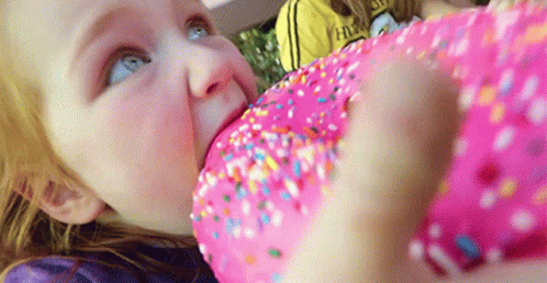 A Little Girl Eating A Pink Donut With Sprinkles GIF