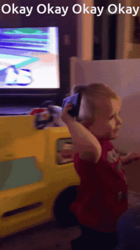 A Little Girl Holding A Cell Phone In Front Of A Tv Screen That Says Okay Okay Okay Okay GIF