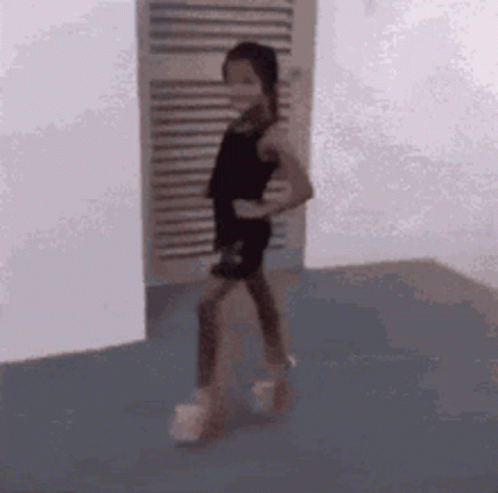 A Little Girl In A Black Dress Is Standing In A Room . GIF