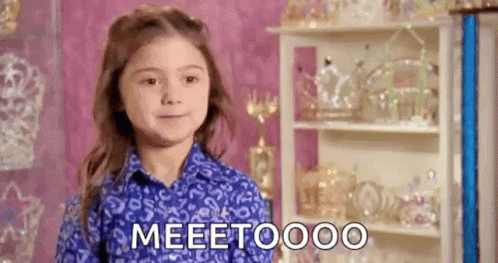 A Little Girl In A Blue Shirt Is Standing In Front Of A Shelf With Trophies And Tiaras . GIF