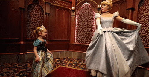 A Little Girl In A Dress Is Standing Next To A Cinderella GIF