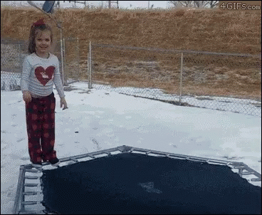 A Little Girl In A Heart Shirt Is Jumping On A Trampoline In The Snow GIF