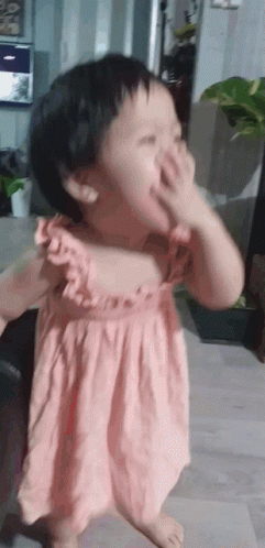 A Little Girl In A Pink Dress Covering Her Face With Her Hand GIF