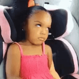 A Little Girl In A Pink Dress Is Sitting In A Car Seat And Making A Funny Face . GIF