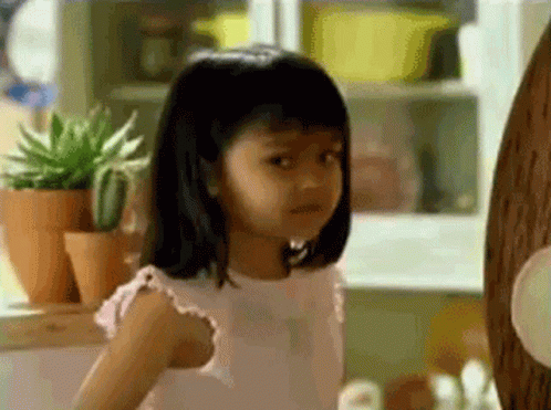 A Little Girl In A Pink Dress Is Standing In Front Of A Wooden Wall . GIF