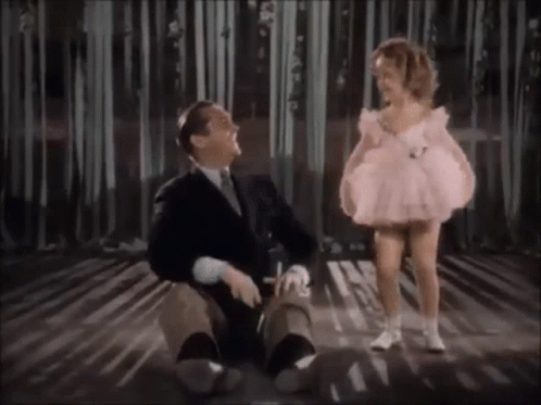 A Little Girl In A Pink Dress Is Standing Next To A Man In A Suit On A Stage . GIF