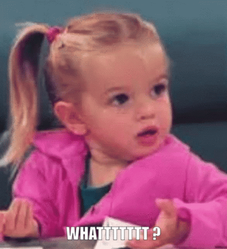 a little girl in a pink jacket is sitting at a table making a funny face and saying what ?