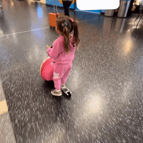 A Little Girl In A Pink Outfit Is Pulling A Suitcase GIF