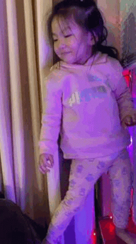 A Little Girl In A Pink Shirt And Pants Is Standing On A Red Carpet . GIF