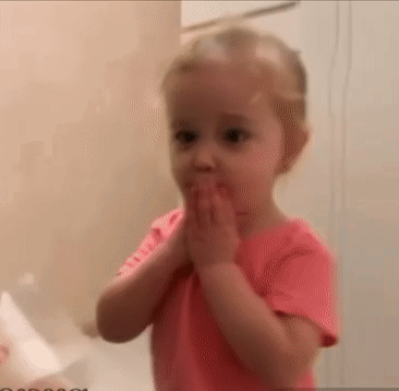 A Little Girl In A Pink Shirt Is Covering Her Mouth With Her Hands In A Bathroom . GIF