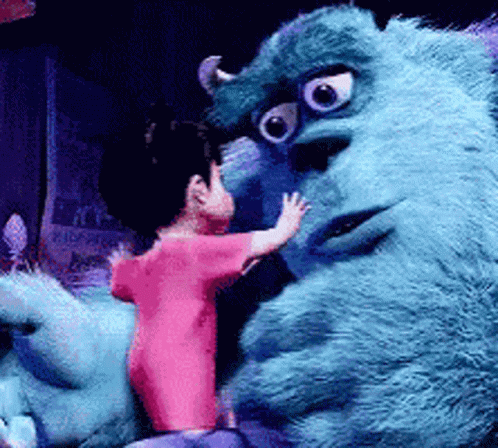 A Little Girl In A Pink Shirt Is Standing Next To A Blue Monster GIF