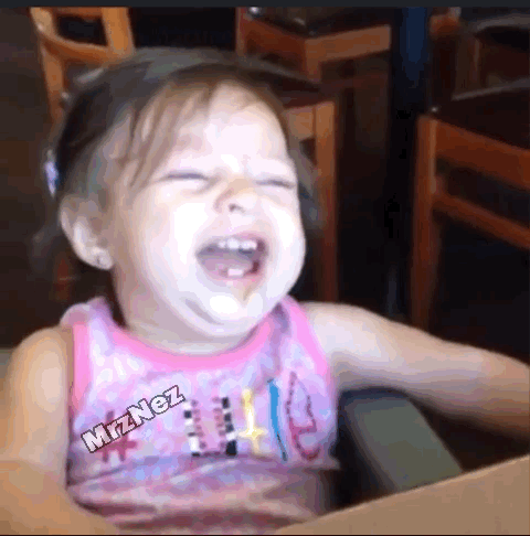 A Little Girl In A Pink Tank Top Is Laughing While Sitting At A Table . GIF
