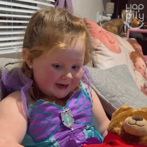 A Little Girl In A Purple And Blue Dress Holds A Teddy Bear GIF