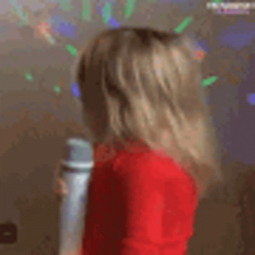 A Little Girl In A Red Sweater Is Holding A Microphone . GIF